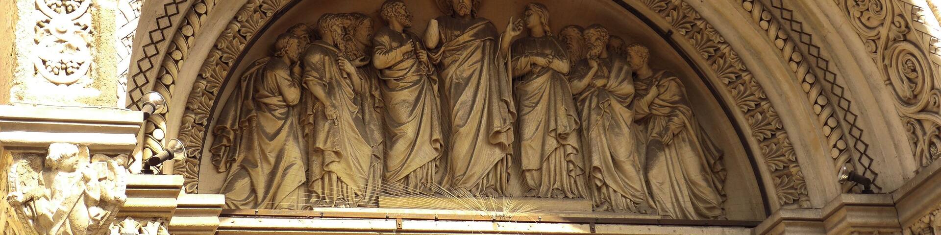 A detailed stone carving of a religious scene with a central figure, surrounded by other figures, within an ornate architectural arch.
