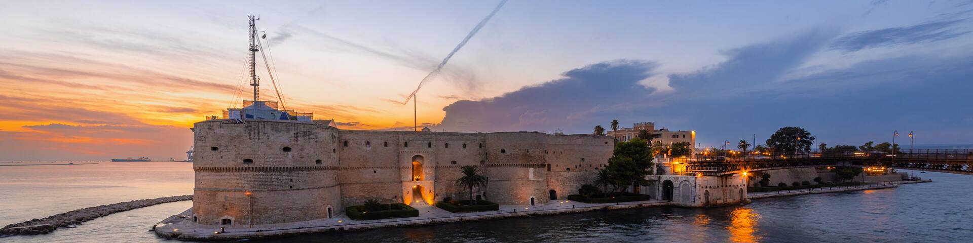 A historic fort with a tower, a calm sea, and a sunset sky.
