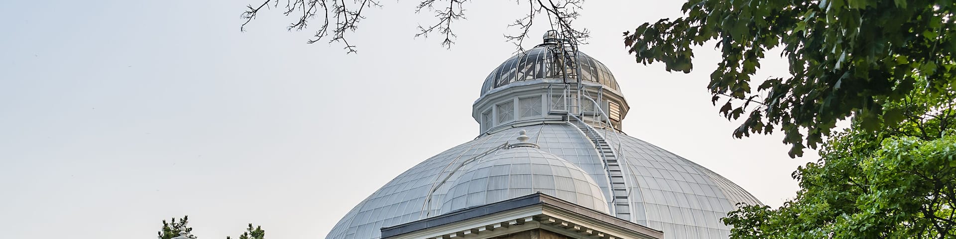 A large glass-domed building with a classical facade, surrounded by lush gardens and a clear sky.
