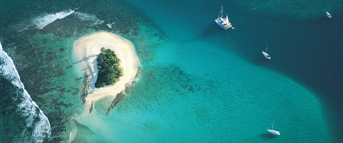 An aerial view of a turquoise lagoon with a small island, clear waters, and several boats.