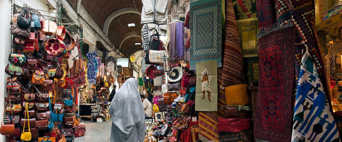 Une rue étroite bordée d’étals où sont vendus des sacs, des chaussures et des articles textiles.