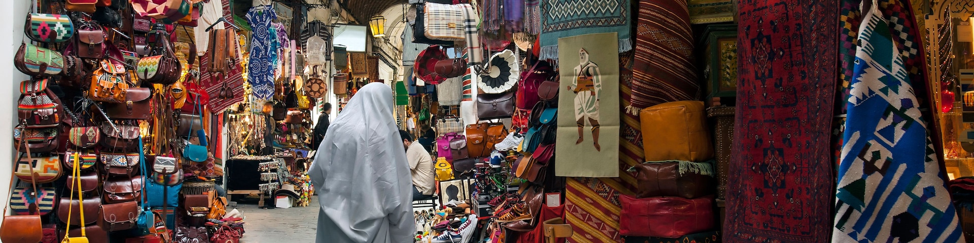 Une rue étroite bordée d’étals où sont vendus des sacs, des chaussures et des articles textiles.
