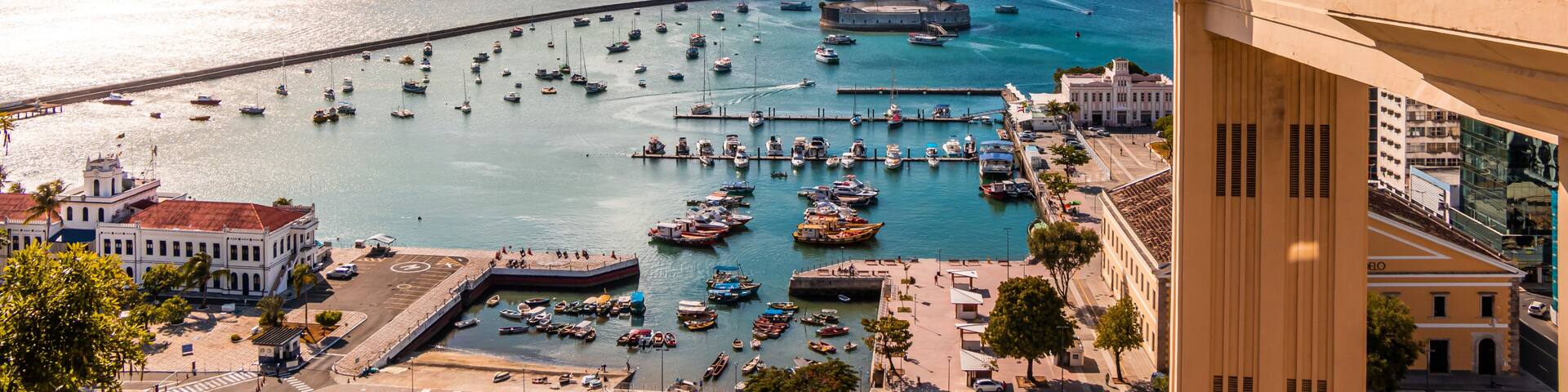 A coastal cityscape with a prominent tower, a marina filled with boats, and a clear blue sky.