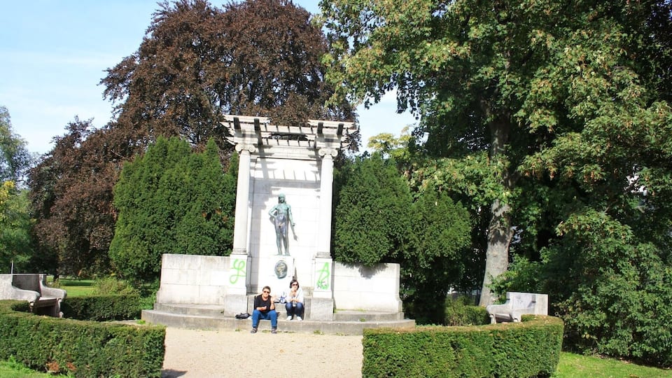 Una estatua en un parque con setos cuidados y árboles al fondo.
