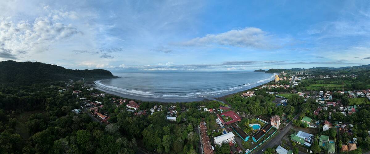 A coastal town with a beach, dense greenery, and a clear sky.