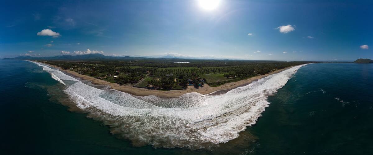 A coastal landscape with a beach, forested area, and mountains in the distance.