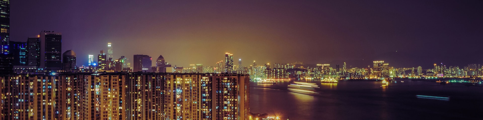 A nighttime cityscape with illuminated high-rise buildings, a river, and a highway.