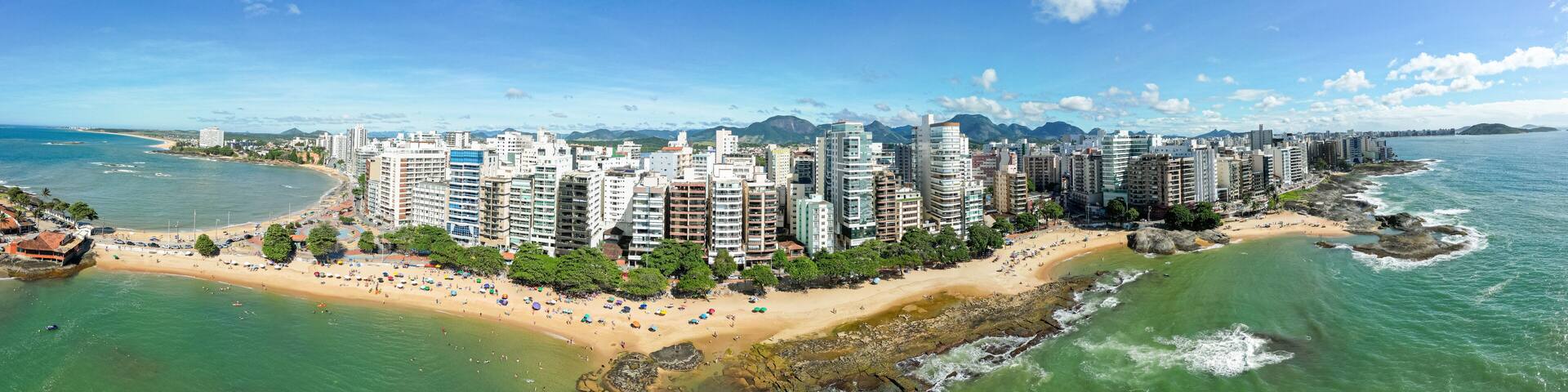A coastal cityscape with high-rise buildings, a sandy beach, and a rocky shoreline.