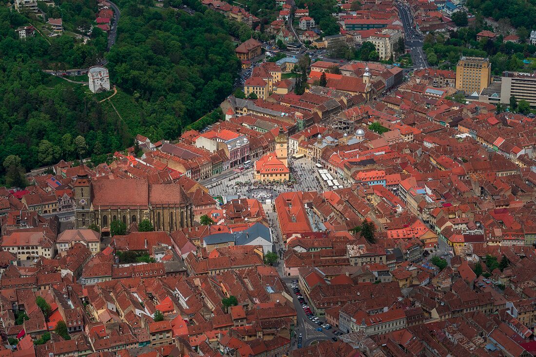 An aerial view of a historic town with red-roofed buildings, a prominent church, and surrounding greenery.