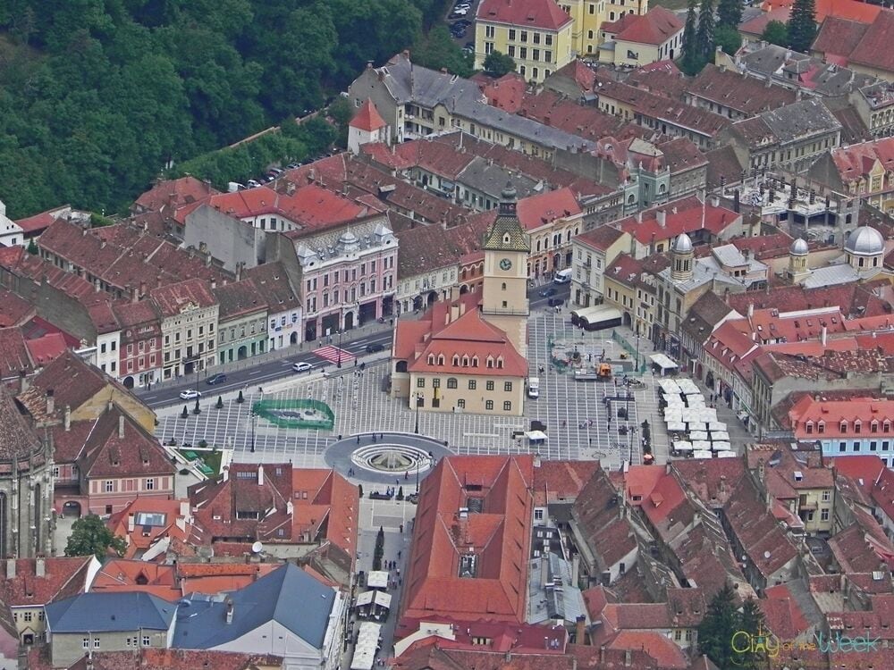 An aerial view of a historic town with red-roofed buildings, a central square, and a prominent clock tower.