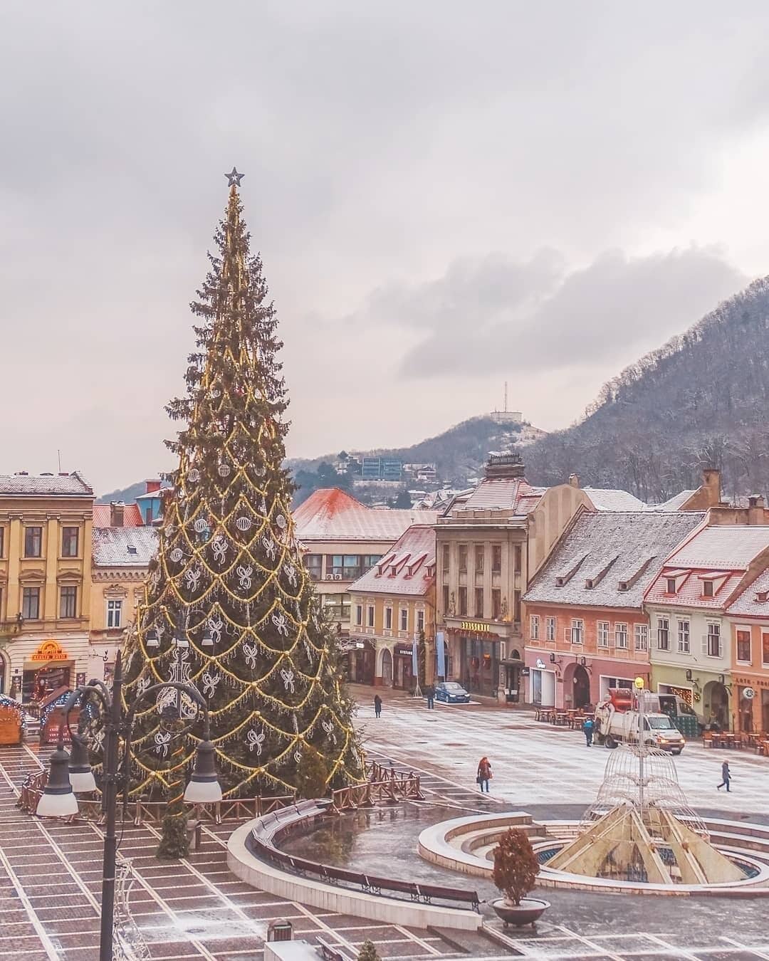A large decorated Christmas tree in a square with buildings and a mountain in the background.