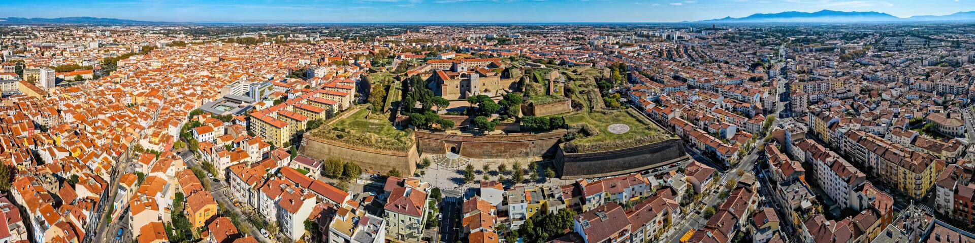 A panoramic view of a city with a prominent historical fortress surrounded by densely packed buildings with red-tiled roofs.