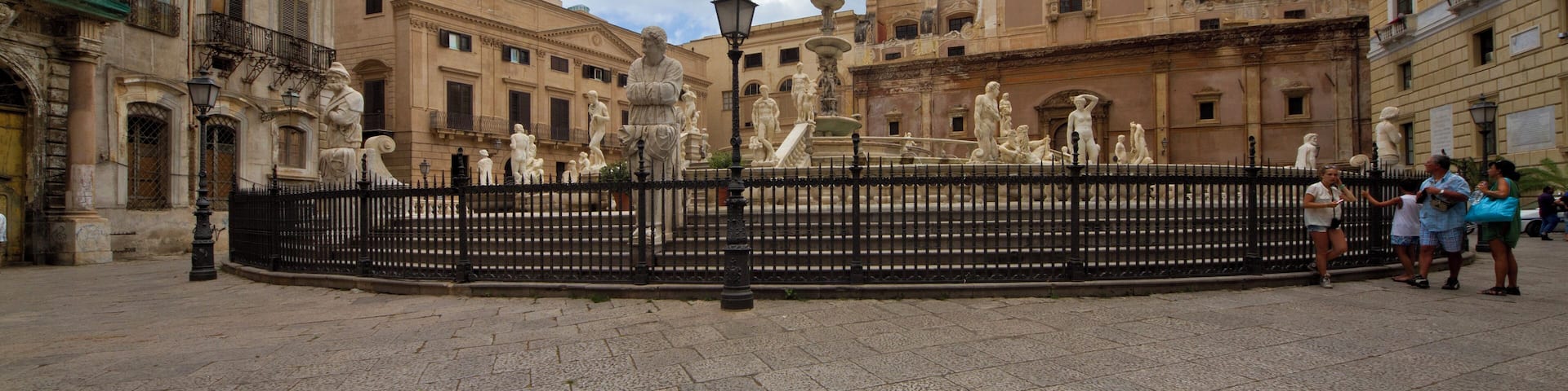 A historic plaza with a fountain, surrounded by classical architecture and a domed building.
