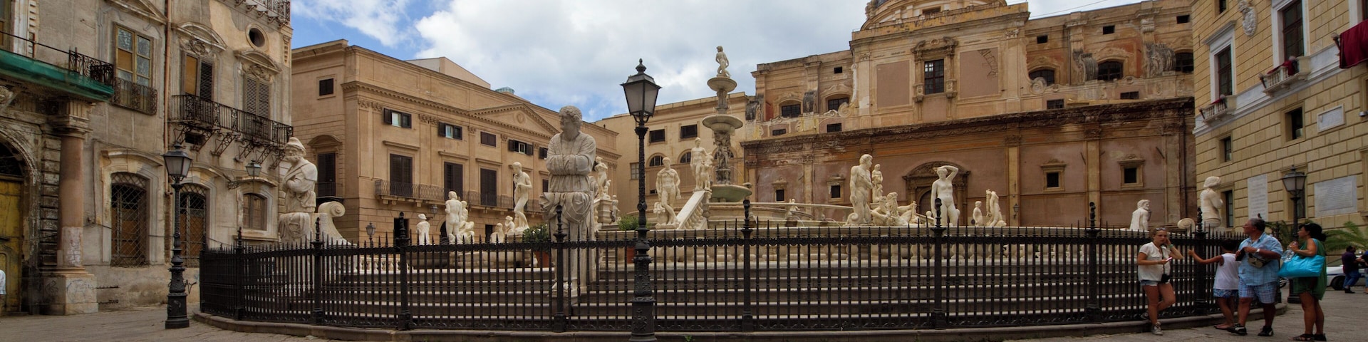 Una plaza histórica con una fuente, rodeada de arquitectura clásica y un edificio con cúpula.