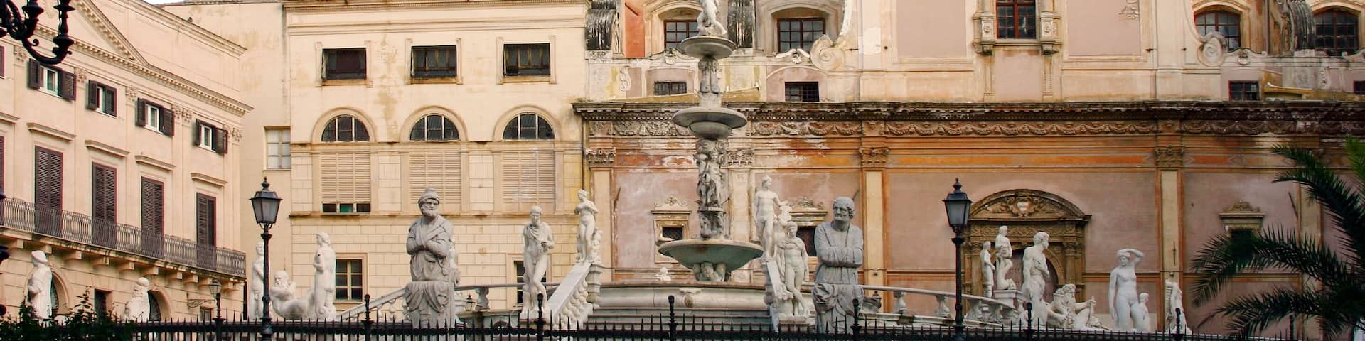 A historic plaza with a fountain, statues, and a domed building.