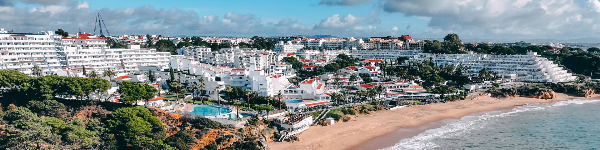 Aerial view of golden cliffs meet the azure sea near Praia da Oura, contrasting with the white buildings of Albufeira, Faro District, Portugal.