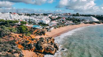 Aerial view of golden cliffs meet the azure sea near Praia da Oura, contrasting with the white buildings of Albufeira, Faro District, Portugal.