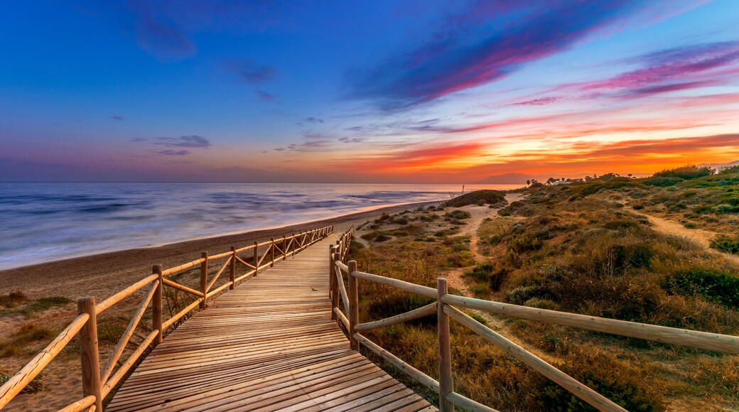 View of amazing bright sundown sky over waving sea and wooden path in countryside in Cabopino, Artola dunes. Marbella, Spain