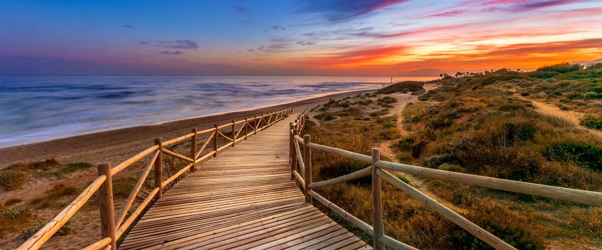 View of amazing bright sundown sky over waving sea and wooden path in countryside in Cabopino, Artola dunes. Marbella, Spain