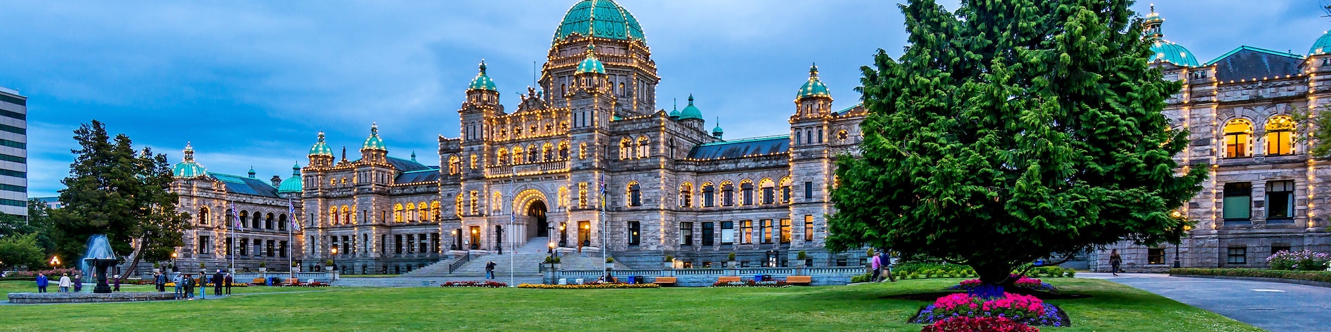 A historic building with a large dome and multiple towers, surrounded by a well-maintained lawn and a large tree.