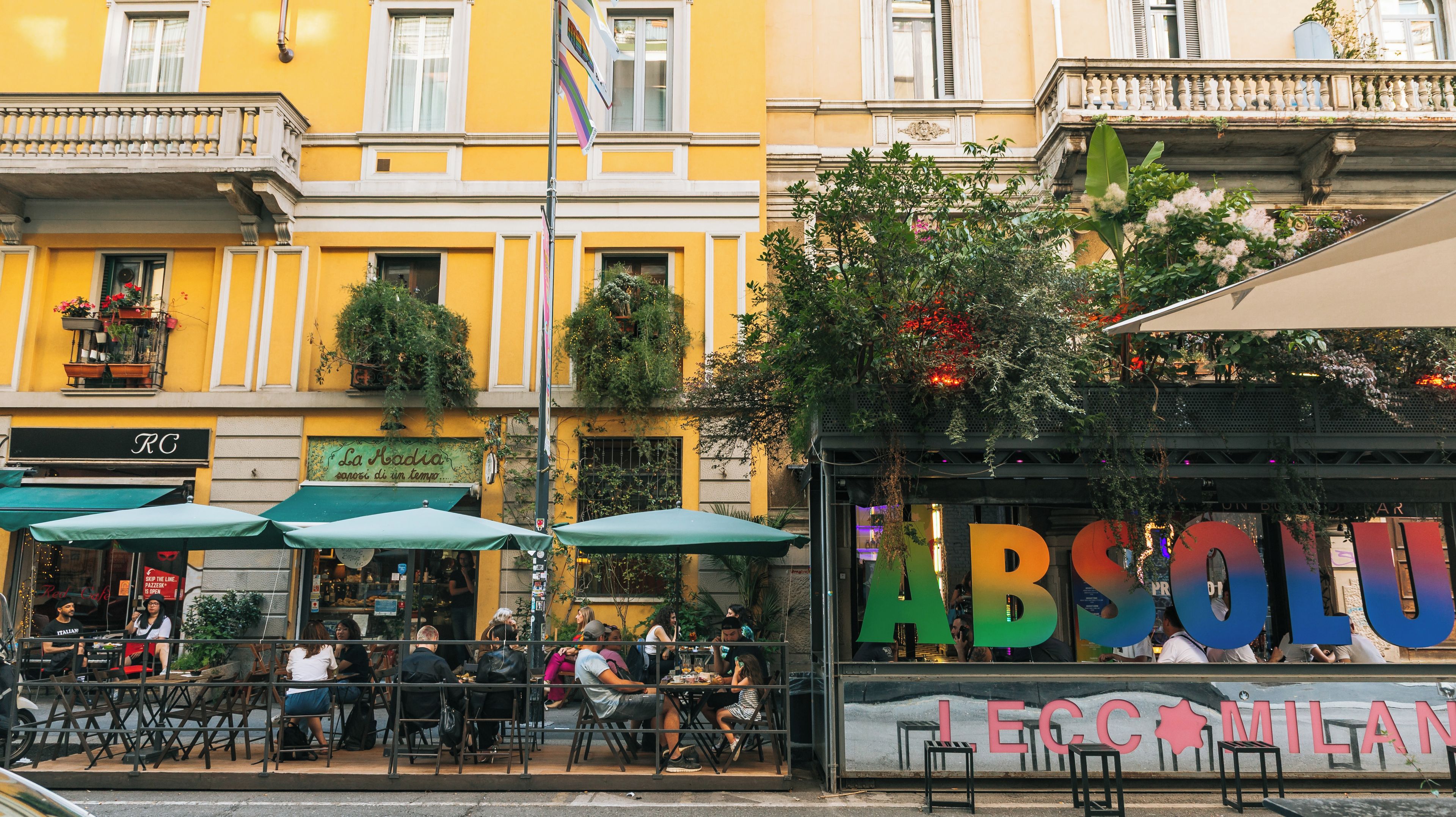 Une rue avec des terrasses, un restaurant appelé « La Radia » et un bâtiment portant l’enseigne « ABSOLU MILAN ».