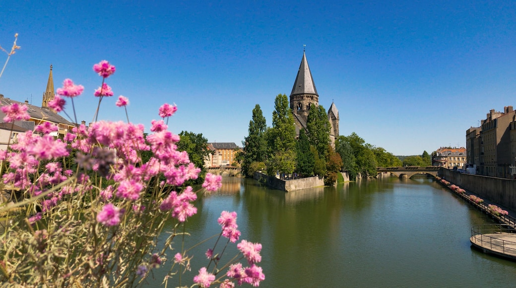 Une rivière avec un pont, le clocher d’une église et des fleurs roses au premier plan.