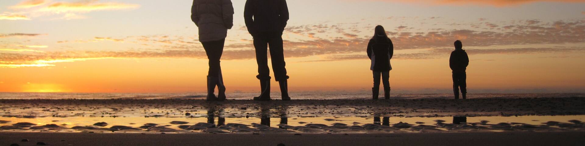A sunset over a beach with silhouettes of people standing.