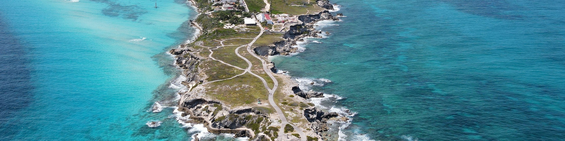 Vue aérienne d’une ville côtière, avec une longue rangée de bâtiments le long du littoral, des eaux turquoise et limpides, et des affleurements rocheux.
