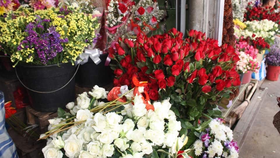Een verscheidenheid aan bloemen, waaronder rode rozen, witte rozen en gele bloemen, op een markt.