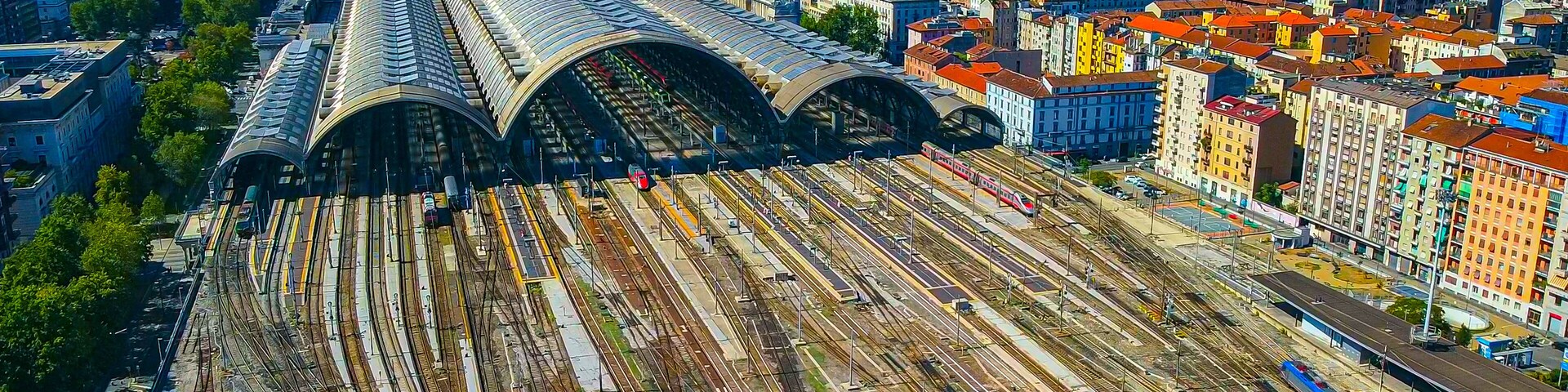 Aerial view of the station where trains arrive. An old arched structure made of metal and glass above the station poles. Tourism. Transport. Skyline with tall buildings. Italy, Milan, 09.2022