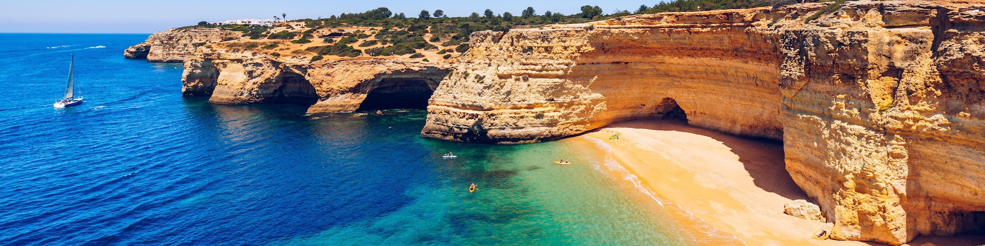 Un paysage côtier caractérisé par des falaises, une eau d’un bleu limpide et une plage de sable.