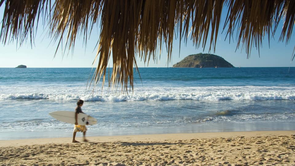 A surfer walking on a beach in Rincon de Guayabitos, Mexico