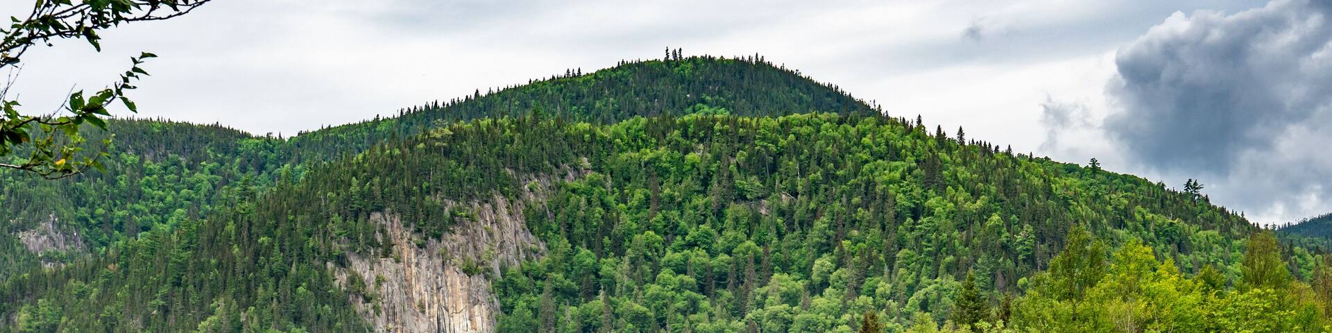 Huge cliffs with green trees everywhere on it facing two dams made by beavers near Fjords du Saguenay in Quebec Province, Canada
