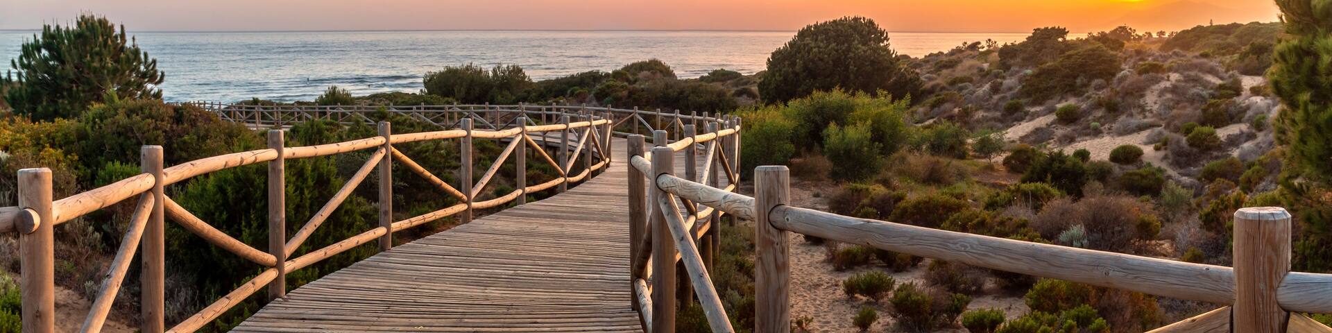 Weathered lumber path leading to calm sea during beautiful sunset in countryside in Cabopino, Artola dunes. Marbella, Spain