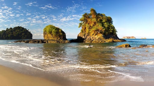A beach with clear waters, rocky outcrops, and lush greenery.