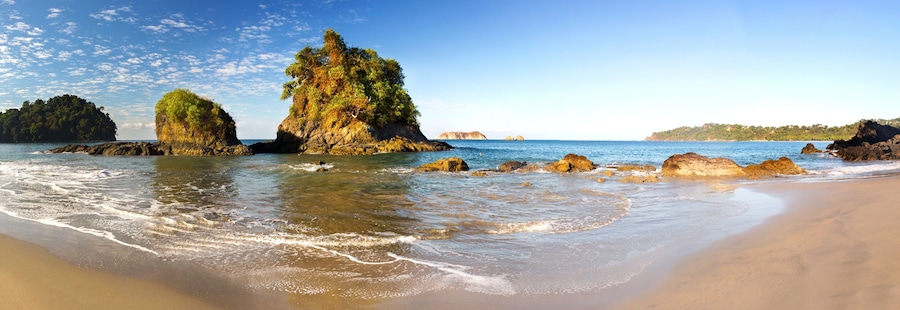 Una playa con aguas cristalinas, afloramientos rocosos y abundante vegetación.