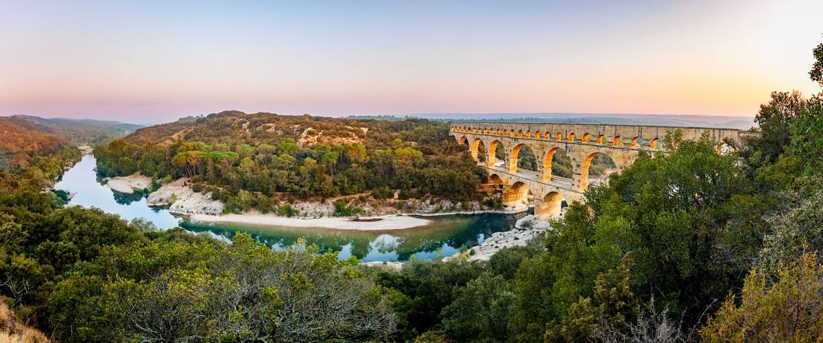 Pont du Gard, ancient Roman aqueduct bridge, elevated panoramic view, river bend and arches, early morning golden light, Gorges du Gardon, natural landscape, UNESCO Biosphere Reserve, Provence, France