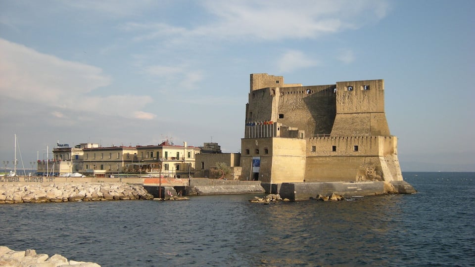 A coastal fortress with a large tower and a fortified wall, overlooking the sea.