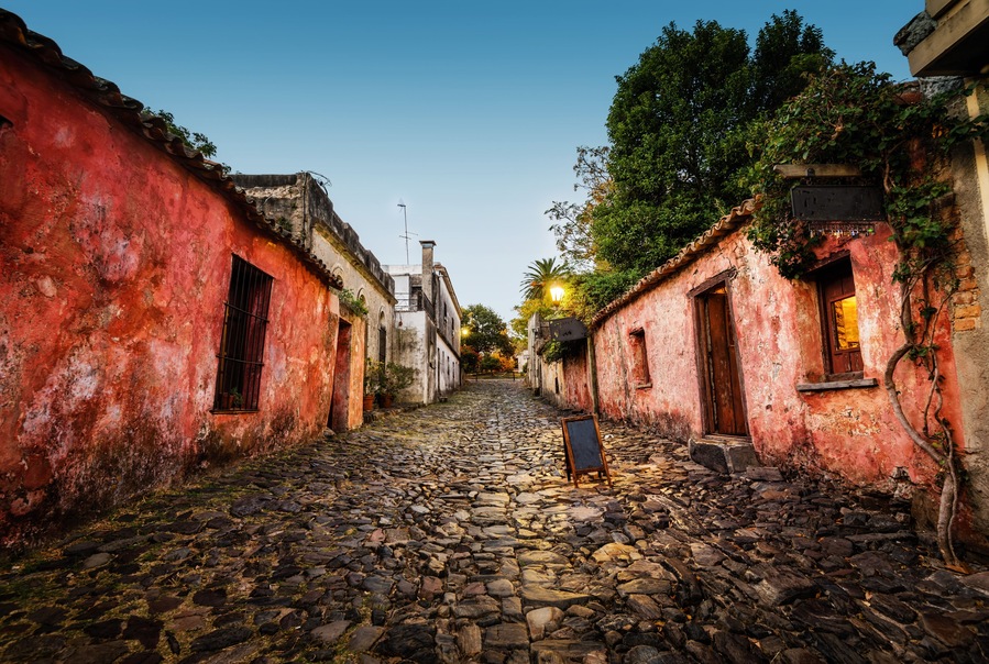 Rua de paralelepípedos ladeada por edifícios antigos com paredes vermelhas e portas de madeira.