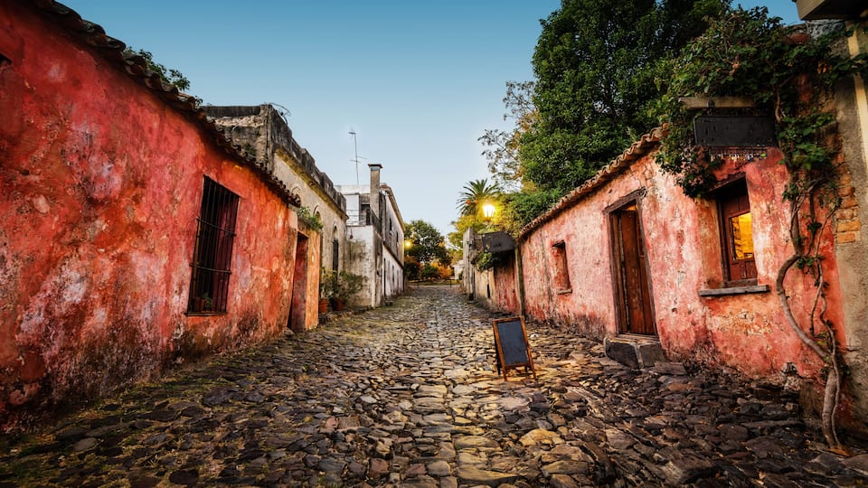 Una calle adoquinada bordeada por edificios antiguos con paredes rojas y puertas de madera.