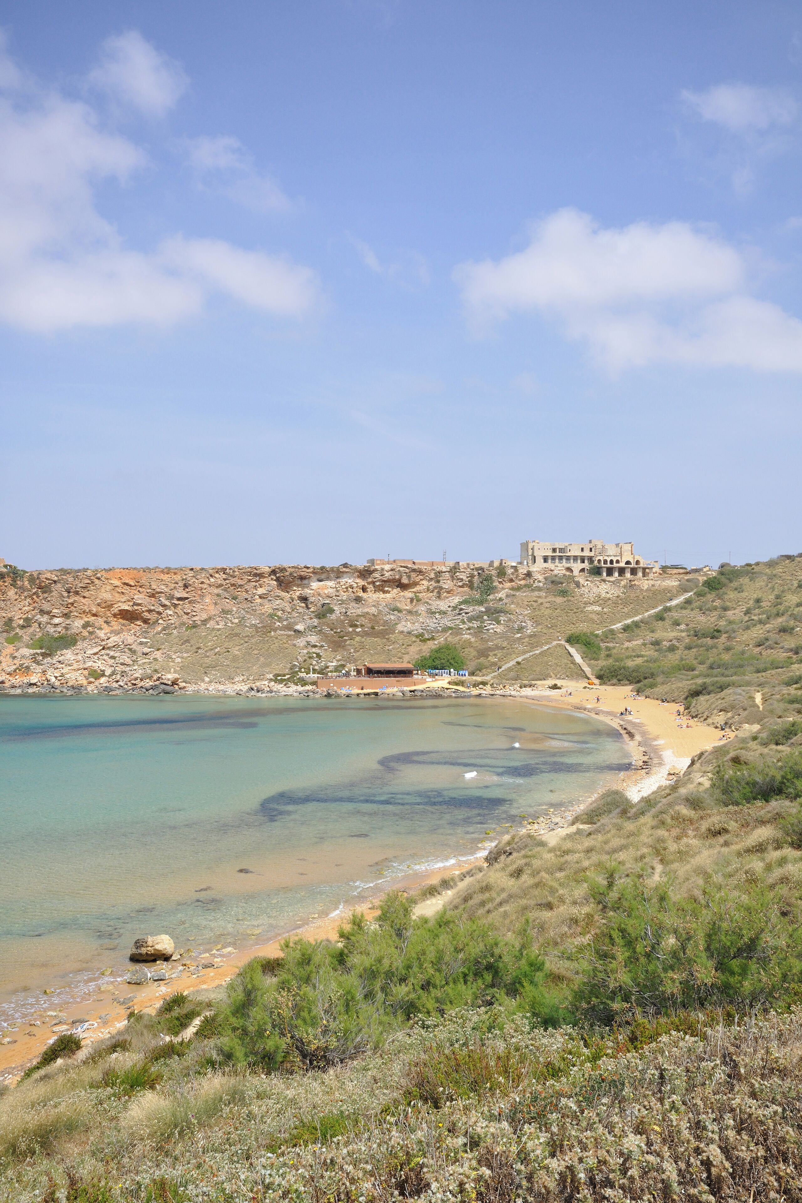 A coastal landscape with a beach, rocky cliffs, and a historic building.