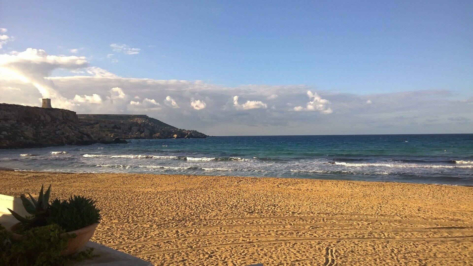 A sandy beach with waves, a rocky cliff, and a tower.
