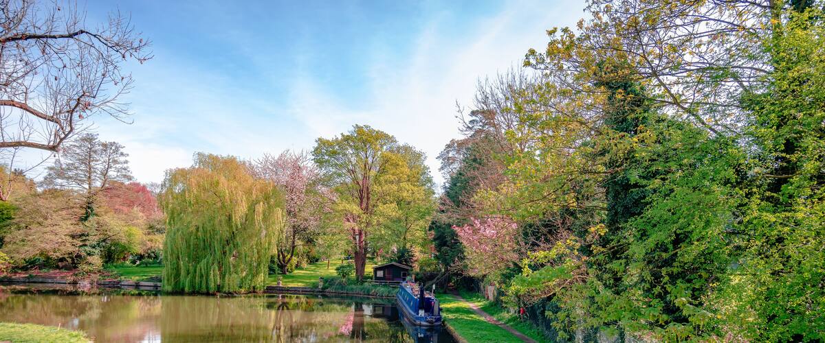 View of river Gade (part of Grand Union Canal), in Cassiobury Park, Watford, Hertfordshire, England. Reflections on water, moored narrow boat.