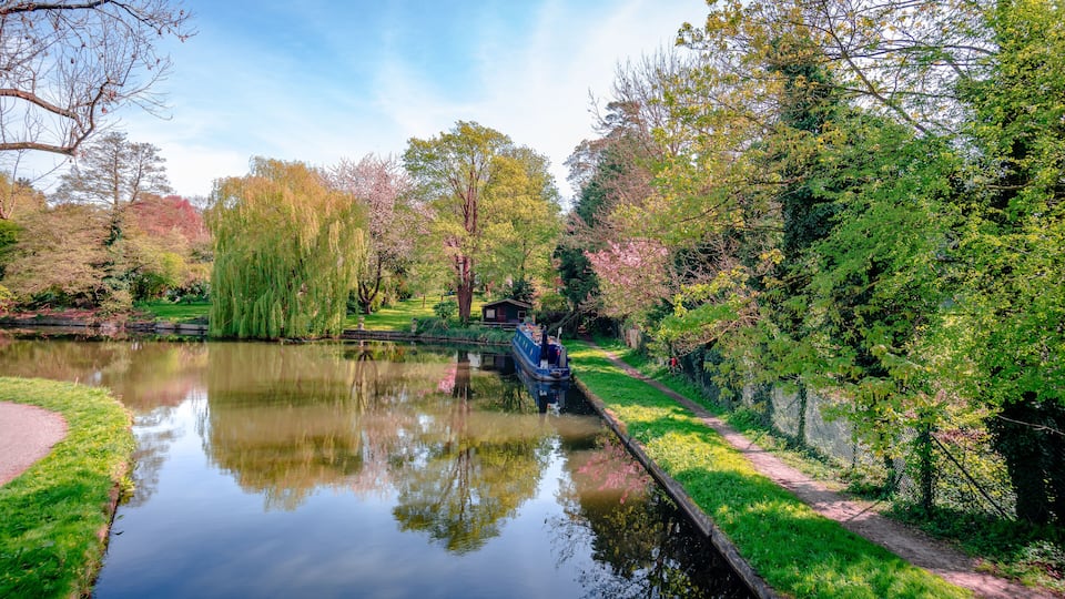 View of river Gade (part of Grand Union Canal), in Cassiobury Park, Watford, Hertfordshire, England. Reflections on water, moored narrow boat.