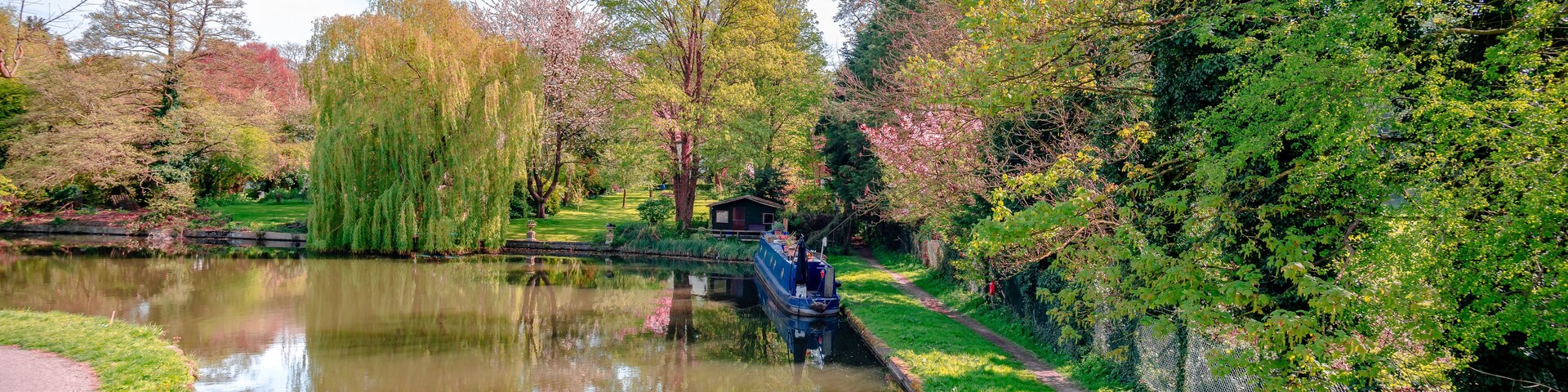 View of river Gade (part of Grand Union Canal), in Cassiobury Park, Watford, Hertfordshire, England. Reflections on water, moored narrow boat.