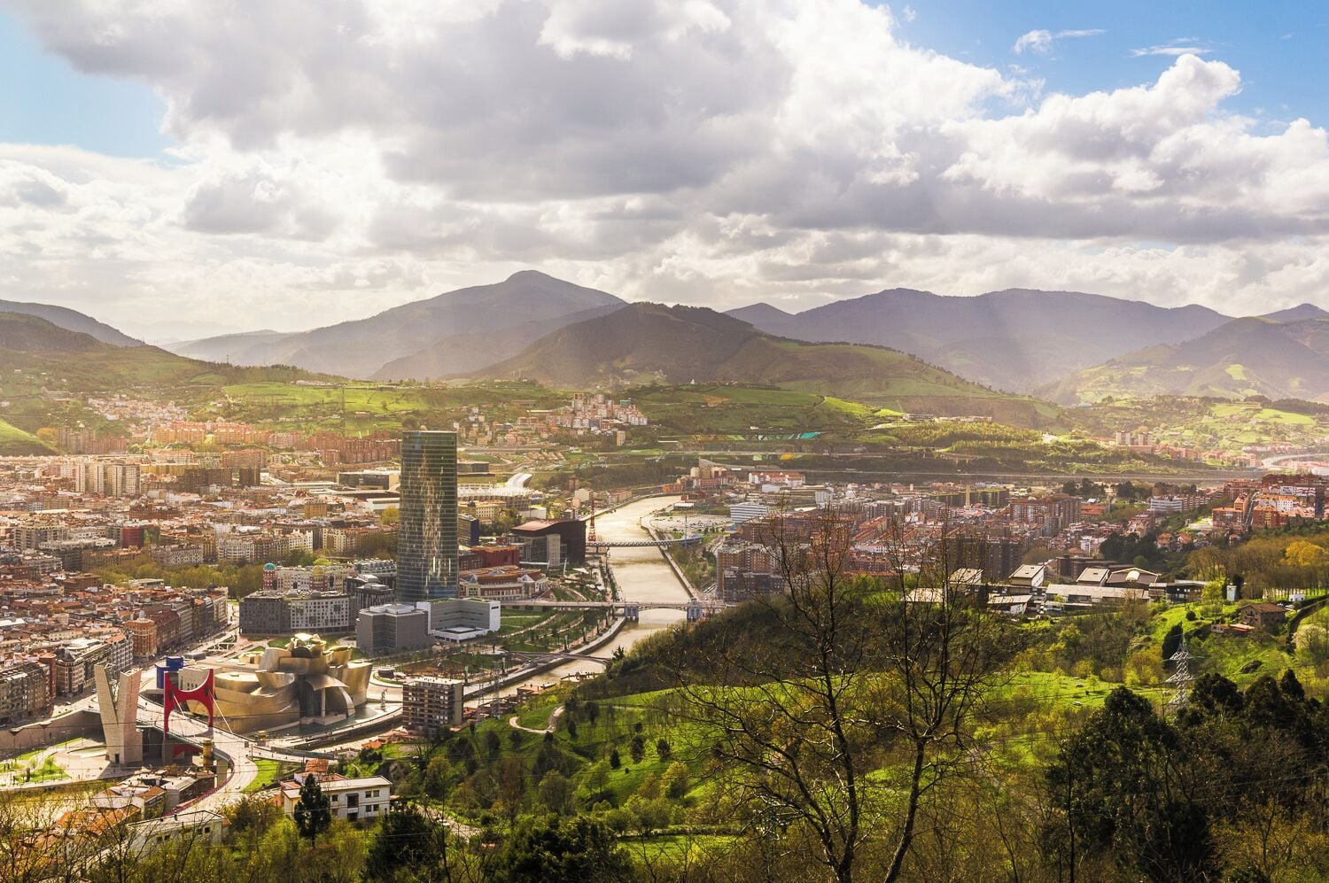 A cityscape with a river, mountains, and a prominent modern building.