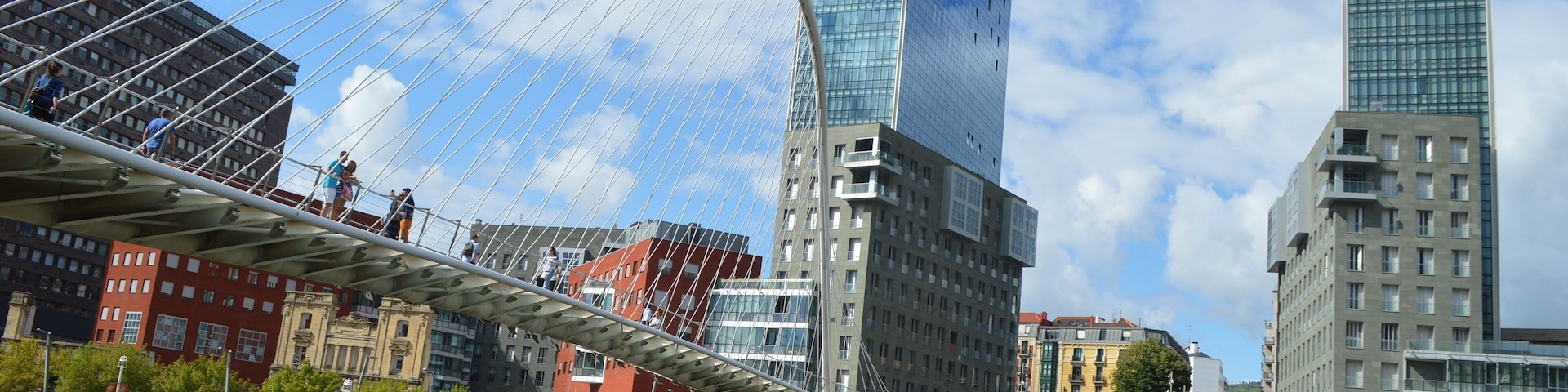El Zubizuri (del euskera "puente blanco"), también conocido como el Puente Peatonal del Campo de Volantín, aunque popularmente llamado puente de Calatrava, es un puente en arco (cuya pista cuelga de él) sobre la ría del Nervión, en la ciudad vasca de Bilbao, en el norte de España. Une el Campo de Volantín (Castaños), en la margen derecha, con Uribitarte (el Ensanche), en la izquierda. Las torres que se ven detrás son las torres Isozaki que son parte de la "Puerta Isozaki" Isozaki Atea (en castellano, "Puerta Isozaki") es como se conoce a un complejo de siete edificios diseñado por el arquitecto japonés Arata Isozaki con la colaboración del arquitecto bilbaíno Iñaki Aurrekoetxea, en el distrito de Abando, en Bilbao, España. Se compone de dos torres gemelas de 82 metros y 23 plantas, y cinco edificios de entre 6 y 8 pisos. Tiene una superficie total de 84.000 m², de los cuales 8.200 m² están destinados a la actividad comercial, mientras que los restantes constituyen 317 viviendas, cuyos precios oscilan entre 400.000 y 800.000€. En el complejo se asientan las sedes de Eusko Ikaskuntza, Unesco Etxea y el Instituto Europa de los Pueblos. Después de haberse intentado por diferentes iniciativas privadas rehabilitar el antiguo Depósito Franco, situado en el Muelle de Uribitarte, y no habiéndose logrado este objetivo, se planteaba un importante y complejo problema urbanístico en Uribitarte. Por un lado, la pasarela Zubizuri diseñada por Santiago Calatrava no conecta exactamente con la zona del Ensanche, donde existe vida cotidiana intensa, creando una barrera física entre ésta y la Ría. Éste es un problema genérico que existe en Bilbao, dado que la ciudad ha vivido siempre de espaldas a la Ría. No existe conexión directa con la Ría, motor de las actividades industriales de la ciudad. Por otro lado, el Ayuntamiento lleva ya varios años con el intento de crear elementos importantes a lo largo de la Ría. Claros exponentes de este criterio son puntos como el Museo Guggenheim Bilbao, el Paseo de Abandoibarra o el Palacio Euskalduna y las demás obras de la Sociedad Bilbao Ría 2000, con el fin de dirigir la recuperación y transformación de las zonas degradadas de Bilbao y su área metropolitana. Así, sumándose a estas construcciones, se pretendía también la construcción de una plaza pública sobre la colindante calle Marina, y resolver así la problemática de un desnivel de unos 14 metros entre la Ría y la zona del Ensanche. Posteriormente, la empresa promotora Vizcaina de Edificaciones de Grupo Urvasco S.A. gestionó con los propietarios del solar sito al otro lado de la calle Marina la realización de una actuación conjunta del área, y el proyecto de la plaza quedó atrás. La nueva solución, expuesta por el arquitecto japonés Arata Isozaki fue diseñar una Gran Escalinata que tiene una anchura de unos 50 metros, en el encuentro con el Paseo de Uribitarte, en equivalencia a la de la Plaza de España en Roma, para conectar estos dos niveles y hacer dos edificios de 23 plantas, unos 82 metros de altura, a ambos lados de la escalinata. Era la propuesta de diseñar una Puerta a Bilbao en el siglo XXI con el fin de conectar el Ensanche y la Ría. De ahí el nombre de las torres, Isozaki Atea, que en euskera significa Puerta Isozaki. Con las torres ya construidas, la elección de diferentes acabados pretende formar un conjunto diversificado y diferenciador respecto a las viviendas masificadas habituales. Se ha empleado vidrio en la fachada de las torres y aplacado de piedras y ladrillo visto o vidrios en los bloques restantes, diferenciando los diferentes volúmenes que componen el conjunto con la textura del material.