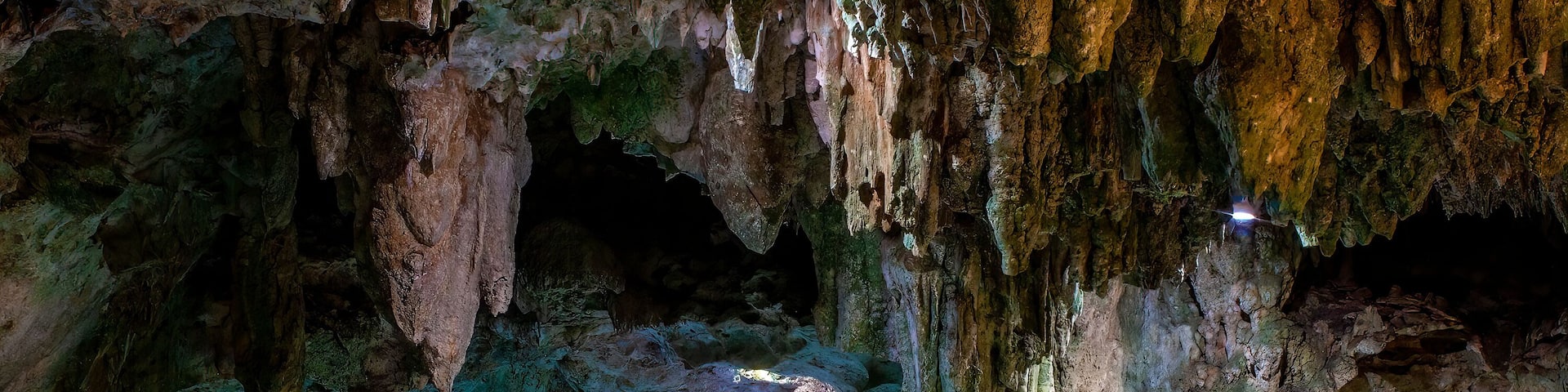 A cave with stalactites and stalagmites, a pool of water, and a narrow passageway.