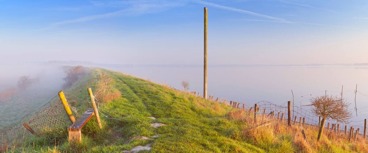 A grassy hillside with a wooden bench, a barbed wire fence, and a clear sky.