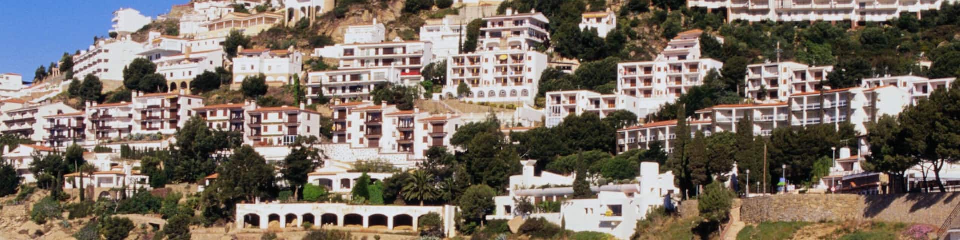 A coastal town with white buildings on a hillside overlooking a sandy beach.